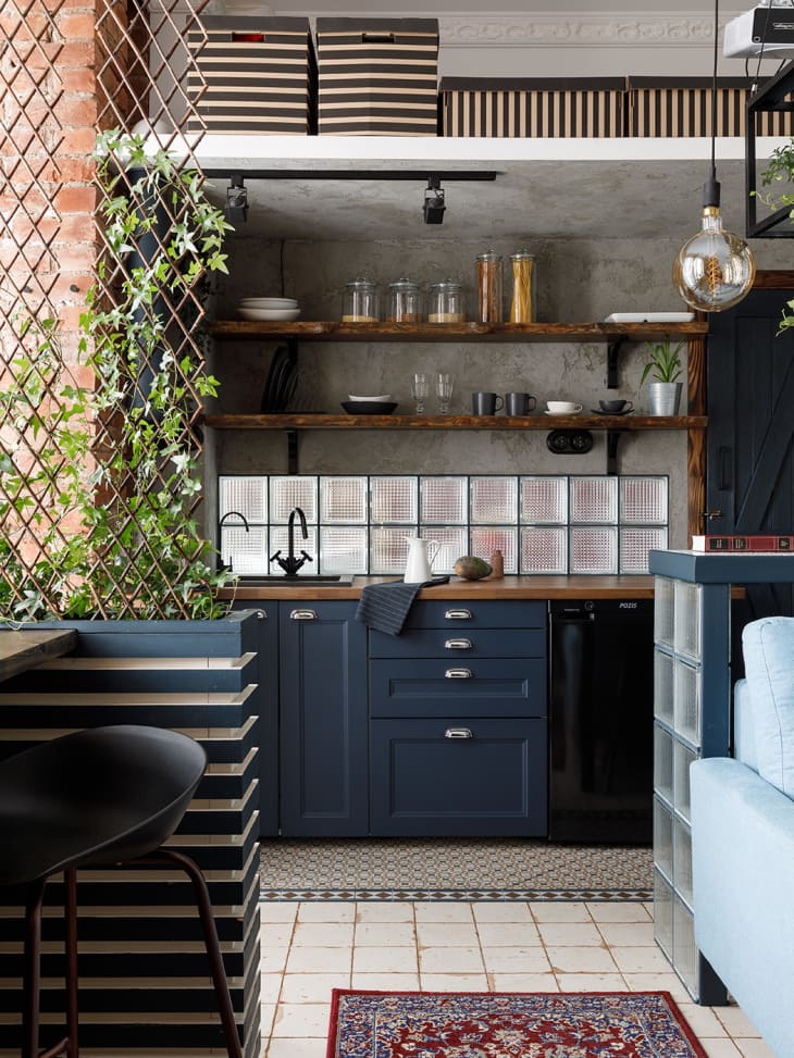 Kitchen with dark blue cabinets, glass block backsplash, open wood shelving, patterned tile floor, exposed brick wall corners