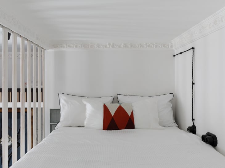 bedroom with white walls, white bedding, white decorative trim, one pillow with deep red accents