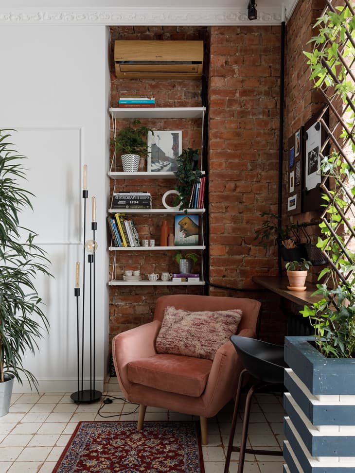 Corner nook with dusty rose accent chair. Exposed brick and white walls, built in black shelves