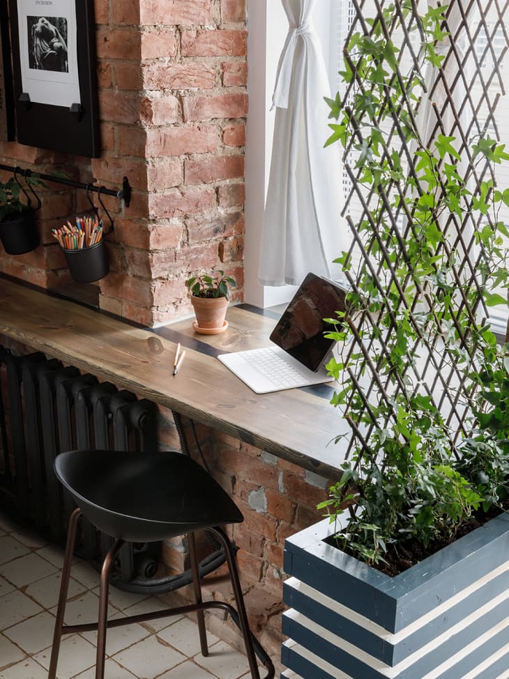 window desk area with exposed brick, laptop, black chair, vine growing on small lattice