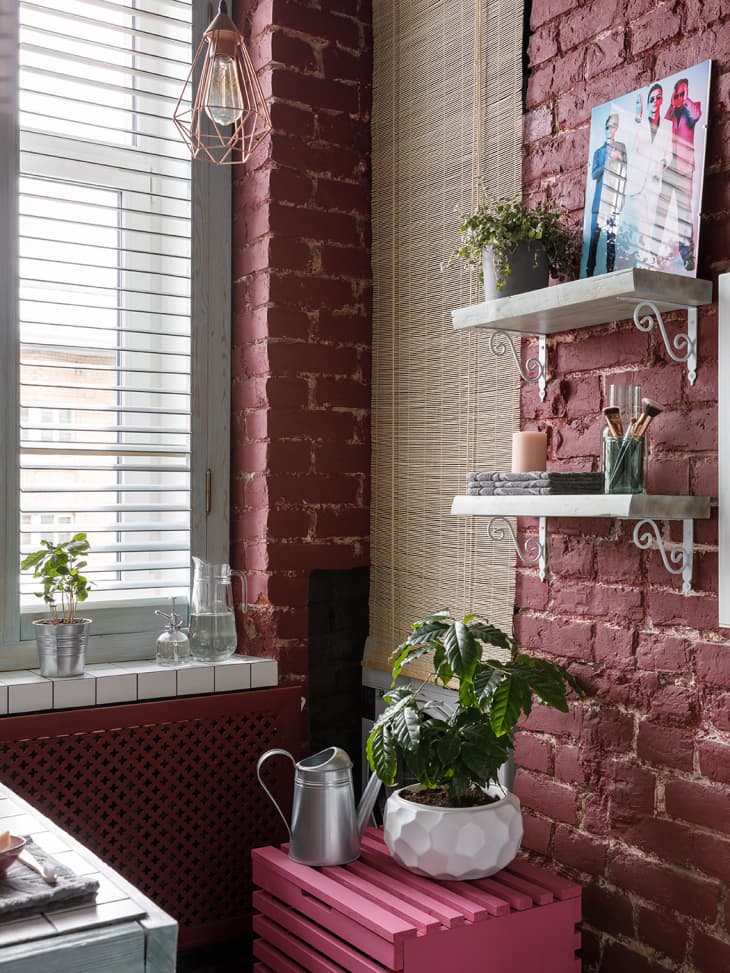 bathroom with painted red brick walls, glass blocks around shower, white tiles, round mirrors, bronze/gold hardware