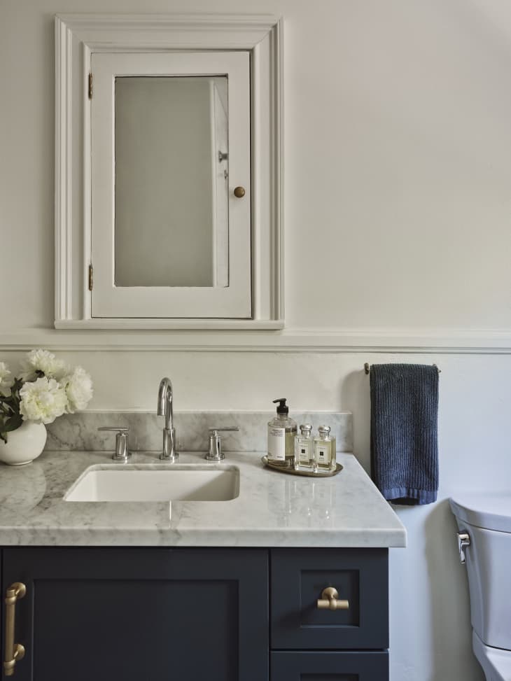 Bathroom with white walls, marble counter and black cabinets. Vase of white flowers on counter