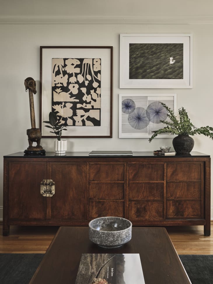 detail of large wood credenza in living room with framed art above, art objects, plant