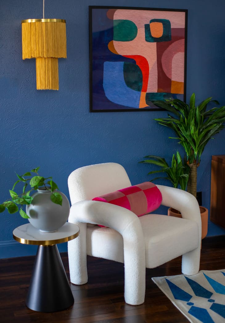 Contemporary white leather armchair with colorful bolster pillow in a dark blue painted living room with splashes of color.