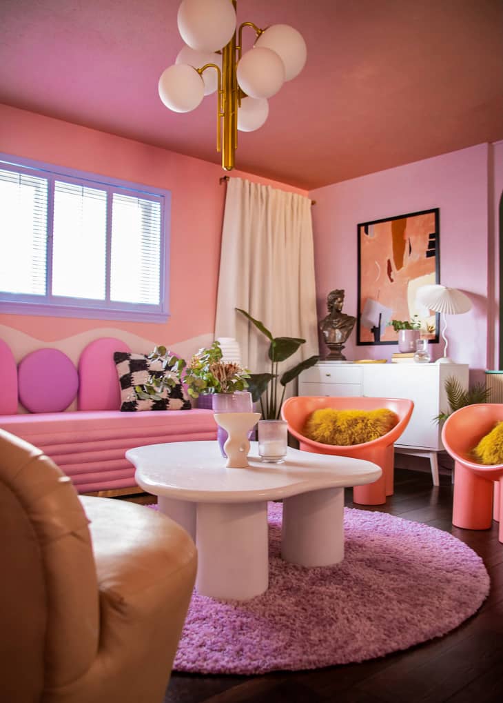 Pink sitting room with multi-light fixture above wavy shaped coffee table.