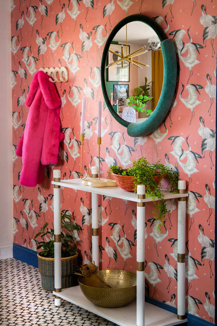 Entryway with colorful pink bird motif wallpaper and a green round mirror above a white console table.