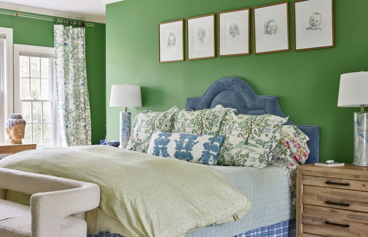 Blue velvet upholstered bed in Kelly green bedroom. Drawings of kids portraits are mounted above bed.