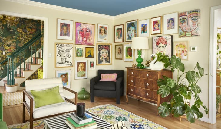 Colorful gallery wall surrounds vintage armchair and wooden dresser in living room.