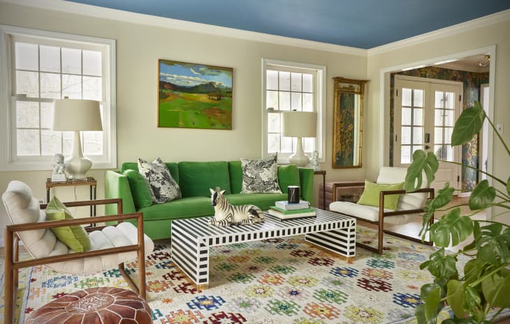 Blue painted ceiling in living room with Kelly green sofa, black and white striped coffee table and two white arm chairs across from each other.