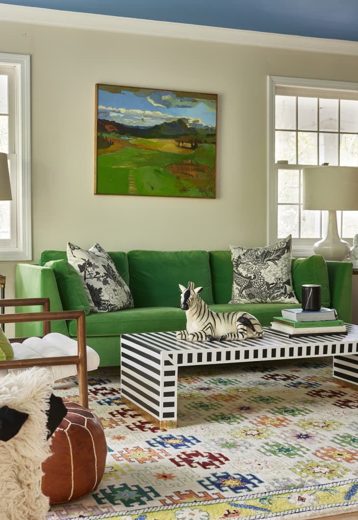Kelly green landscape painting mounted above Kelly green velvet sofa in living room with lots of pattern and texture.