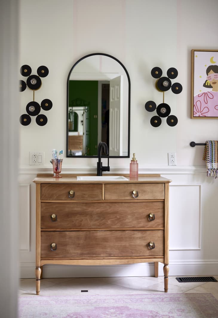 Wooden vanity in bathroom with rounded mirror mounted above.