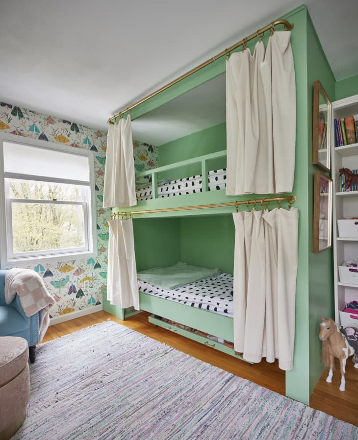 Custom green bunkbeds with brass railing for cream colored curtains.