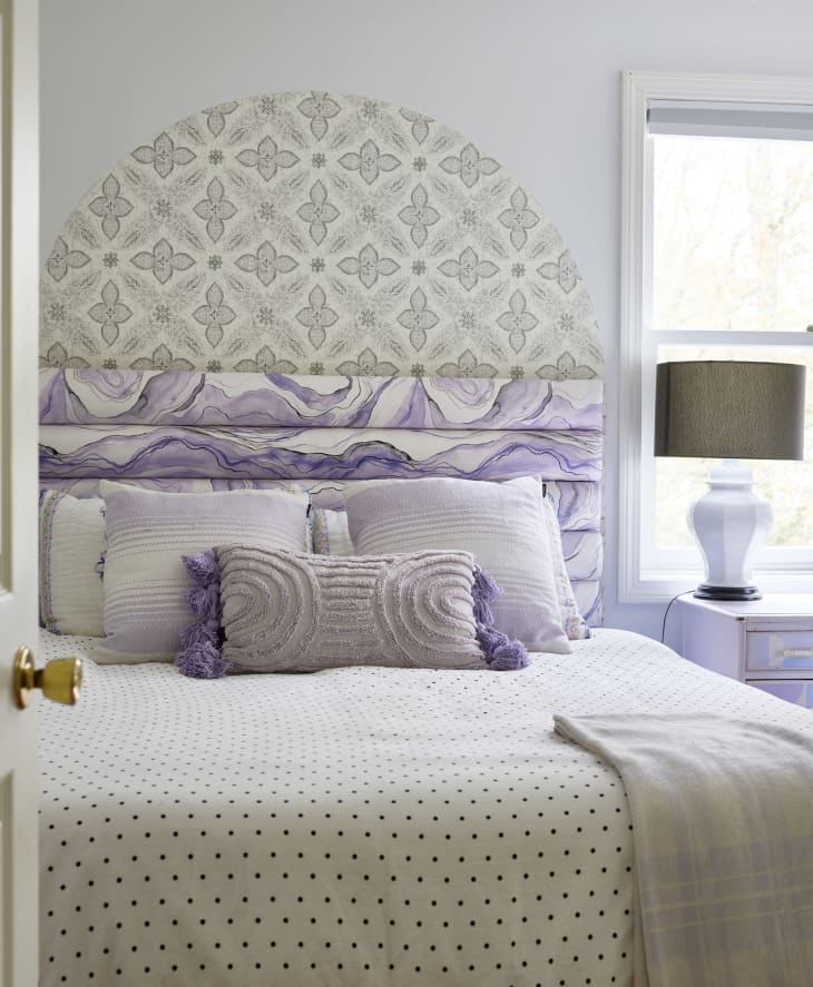 Wall decal above purple and white upholstered headboard in bedroom with bed made neatly with black and white polka dot duvet.