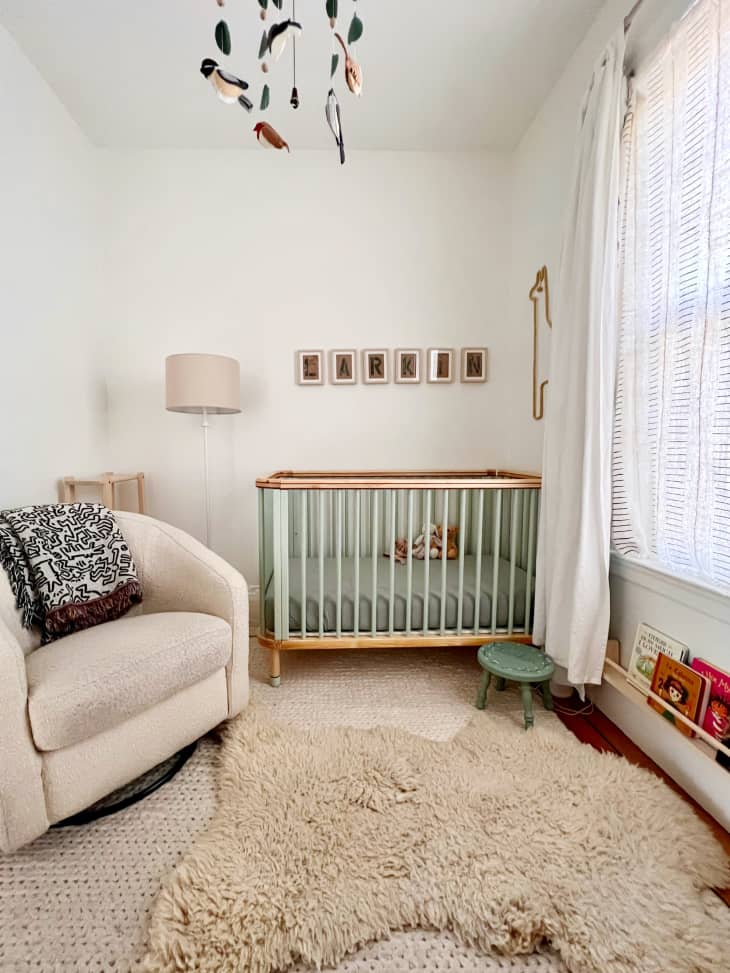 nursery with pale sage green crib, faux tan bear rug, pale sand colored armchair, mobile on ceiling