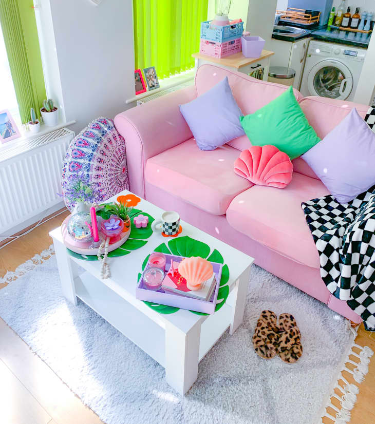 Pastel pink sofa in colorful living room. Monstera place mats on small white coffee table.