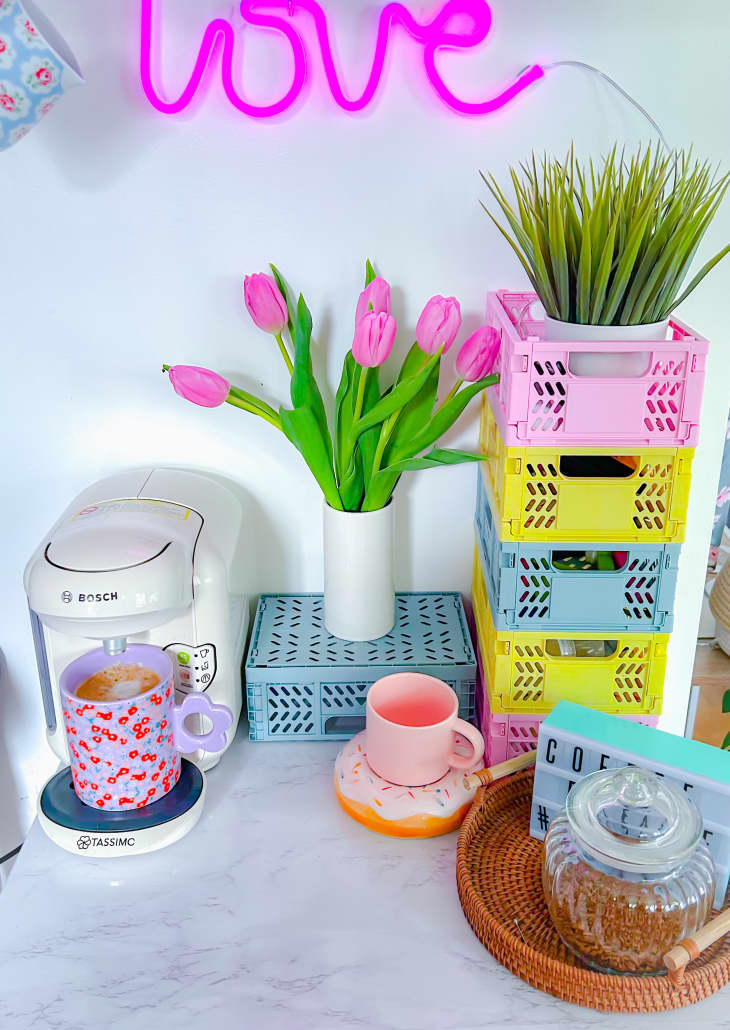 Tulips on surface filled with colorful storage crates and a coffee maker. Neon "Love" sign in the background.