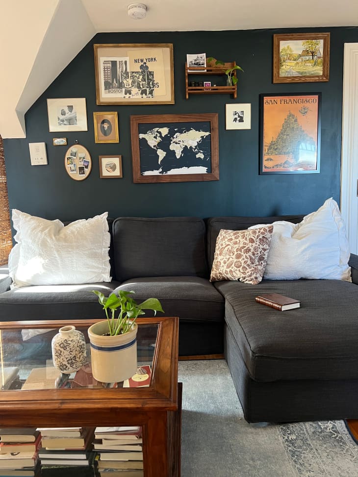 Dark blue painted living room with lots of art prints on the wall and a grey sectional sofa.
