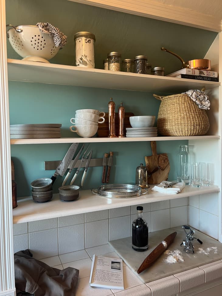 Open shelving kitchen with green painted backdrop. Shelving filled with kitchen tools.
