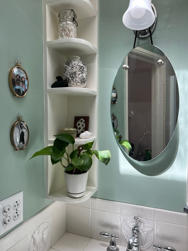 Light green painted bathroom with decor filled open shelving in studio apartment.