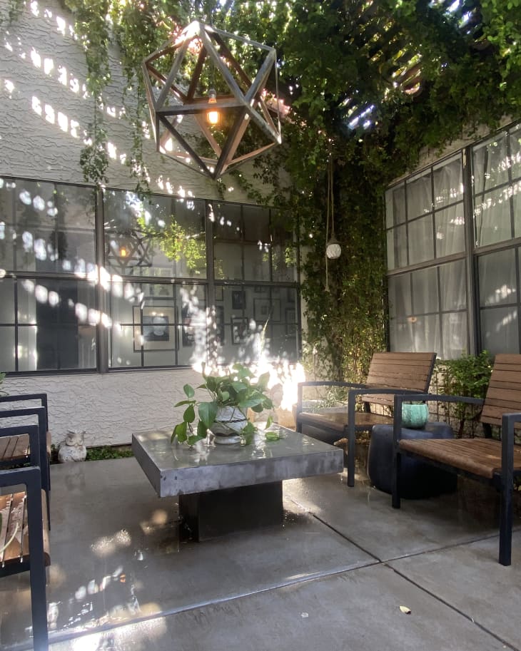 Patio with brown and black chairs, stone table, large geometric pendant light, plants overhead