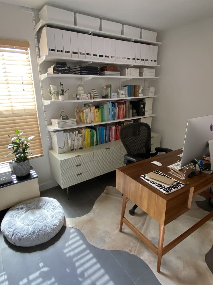 office/home workspace with wood desk with large computer monitor, hide rug, tall white shelves with books, organizing bins up top