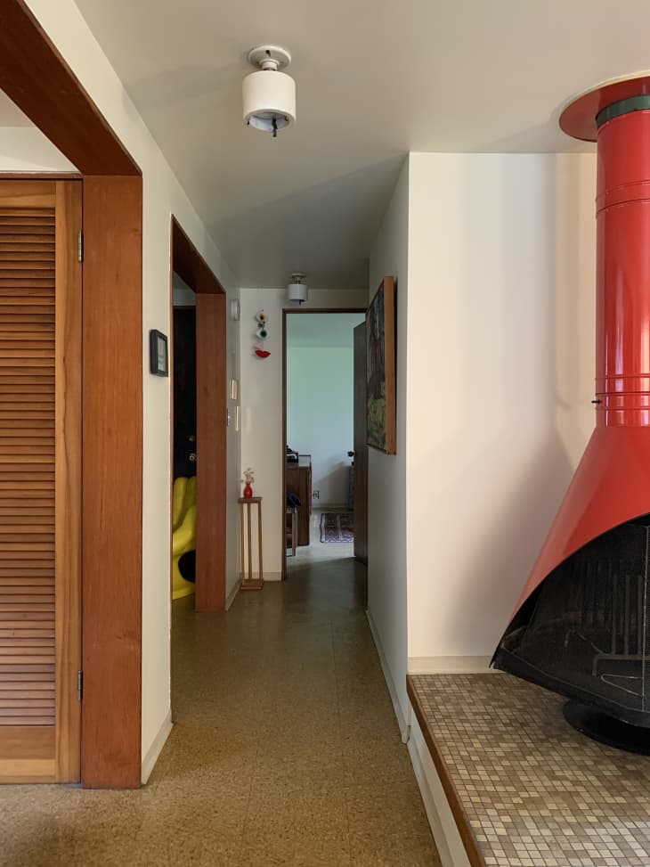 Hallway with white walls, wood trim, wood door, red/orange metal fireplace