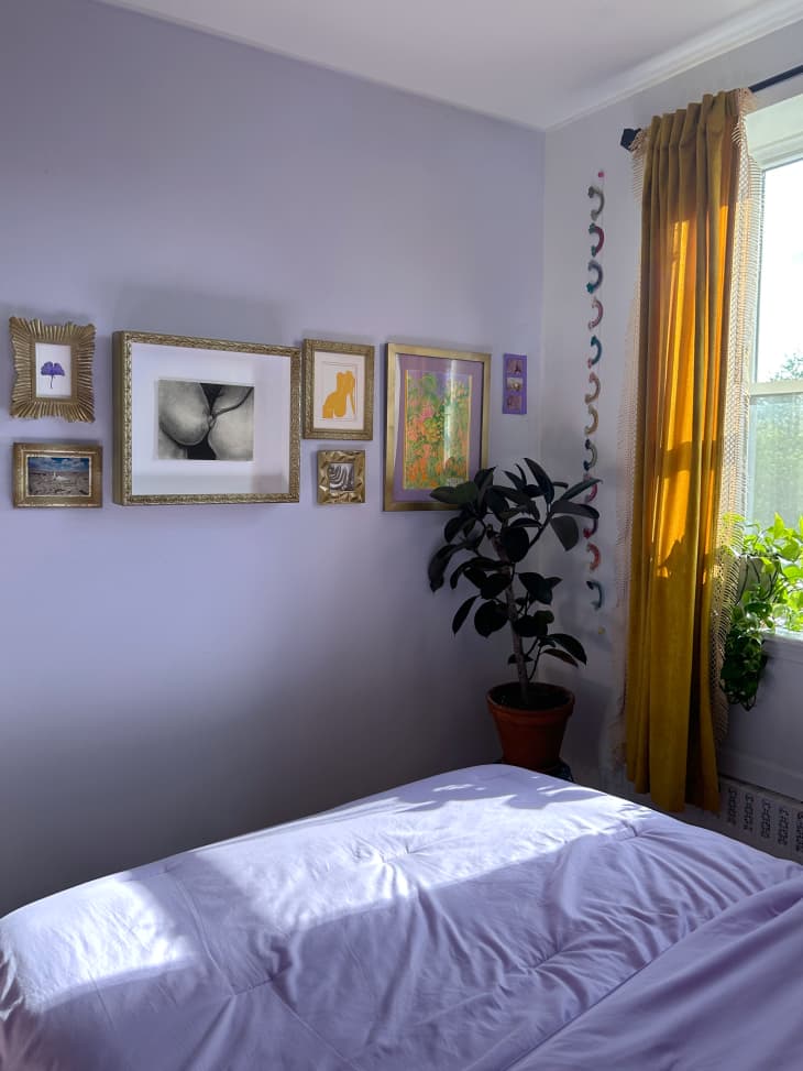 Bedroom corner with lavender painted walls, yellow curtains, and a long gallery wall of art hanging on the wall