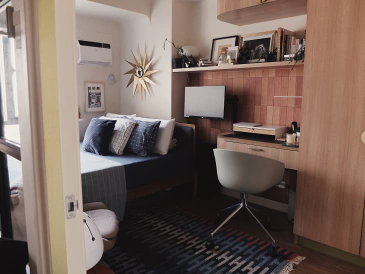 Small desk next to neatly made bed in studio apartment.