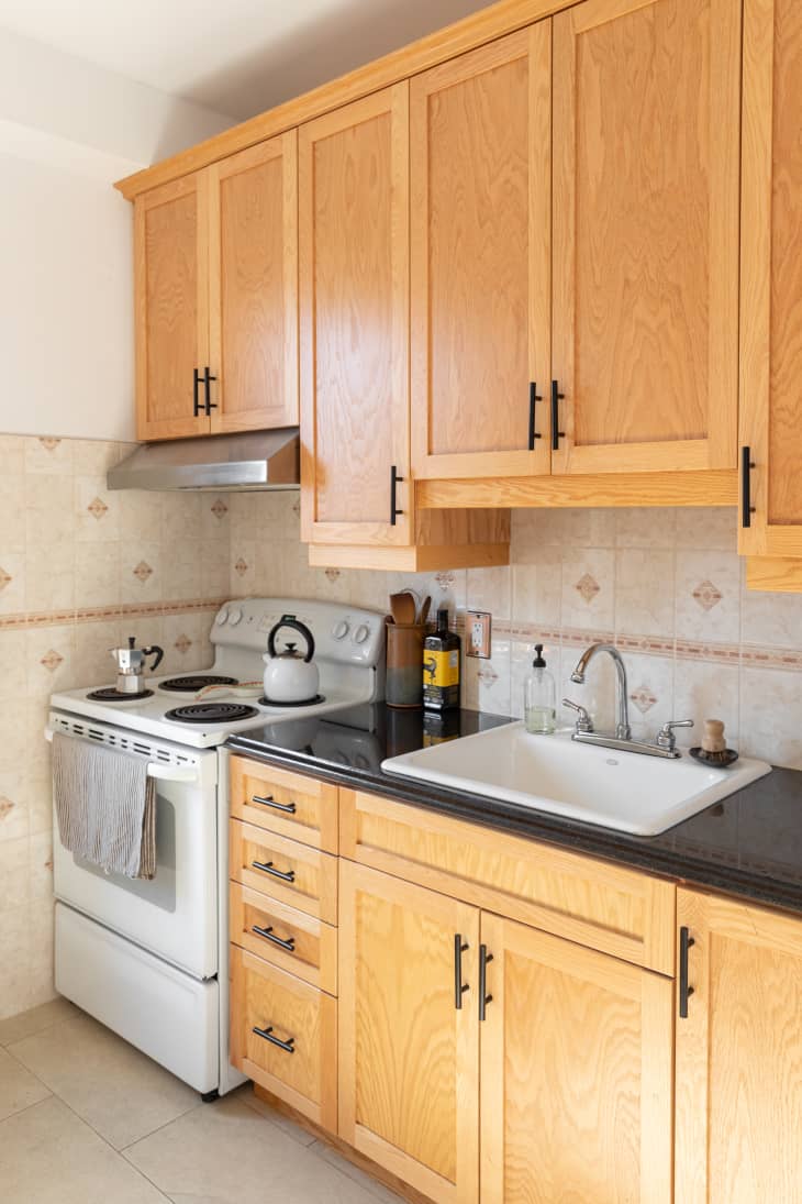 Rental kitchen, with oak wood cabinets, beige wall tiles, and white walls.