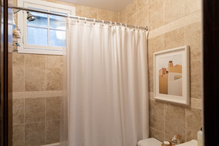 Rental bathroom with beige wall tiles and a white shower curtain.