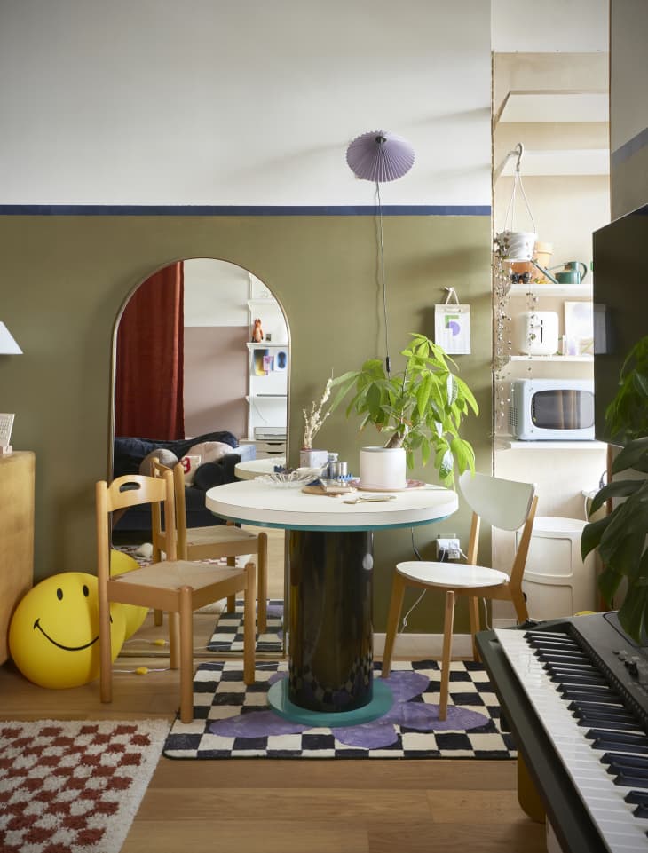 dining room with round table, midcentury style chairs, arched mirror, olive green wall, checkered area rugs, musical keyboard in foreground