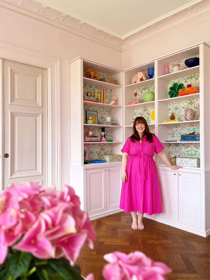 woman in bright pink dress in from of bookshelves in her home