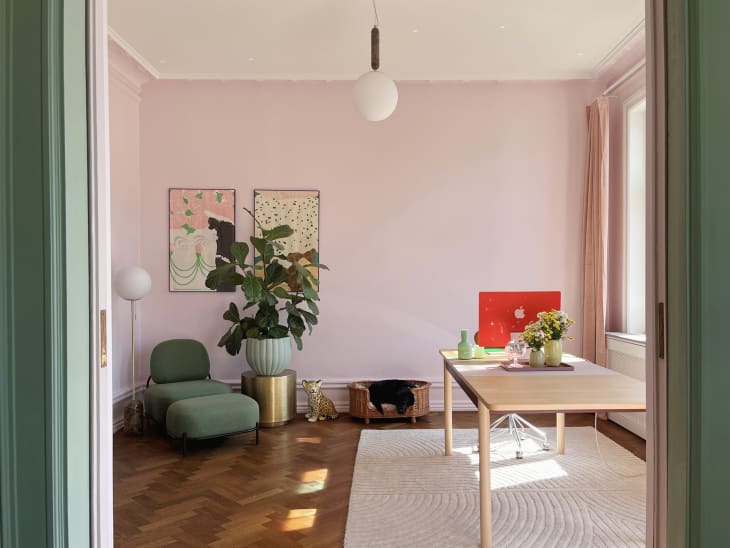 workspace/office with pale pink walls, parquet wood floor, large work table, green lounger chair, large potted plant on gold stand next to dog bed