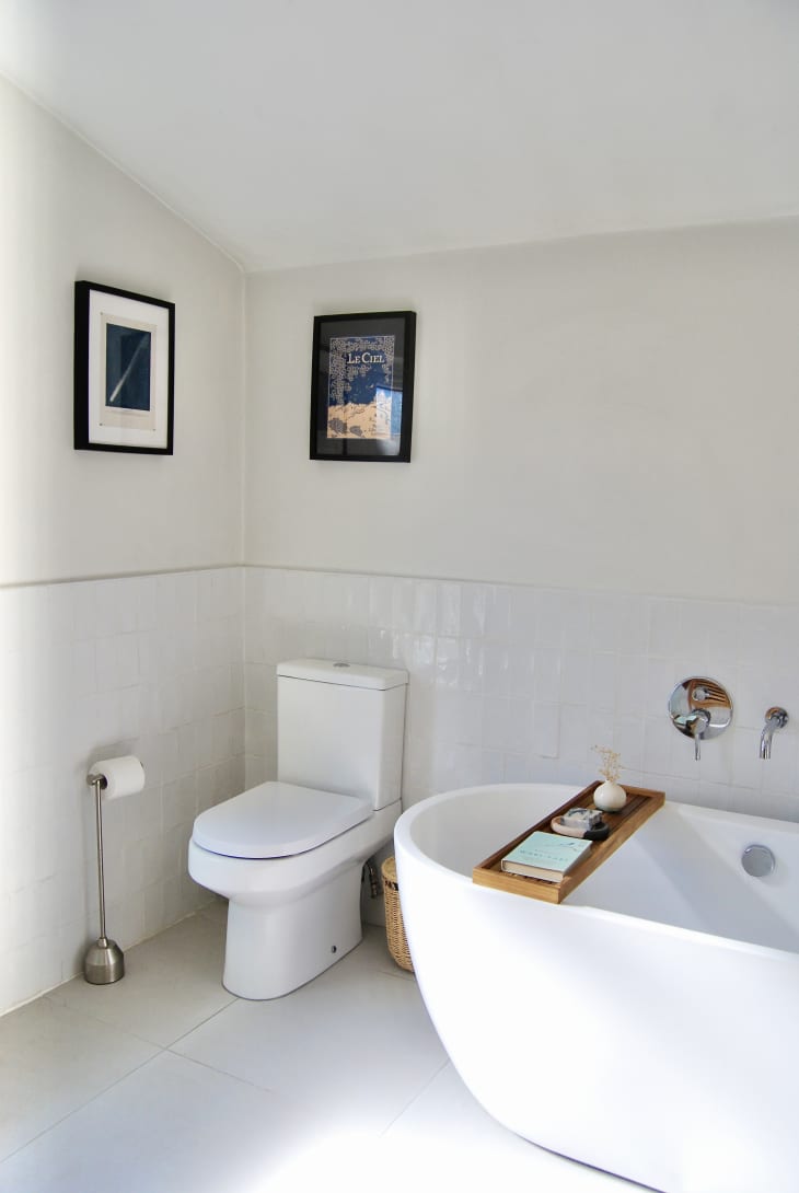 All white bathroom with white tiled wainscoting and a few small art prints mounted on wall.