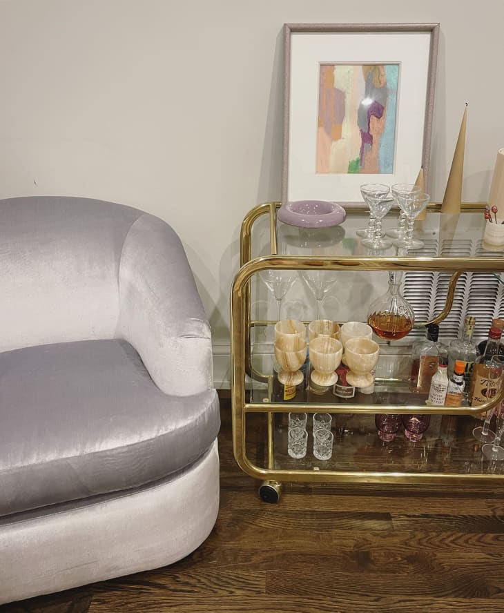 white velvet armchair next to a gold and glass bar cart, wood floor