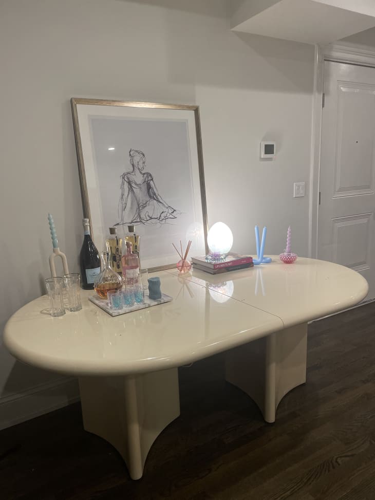 white oval table with marble cocktail tray, bottles of spirits, wine, framed sketch
