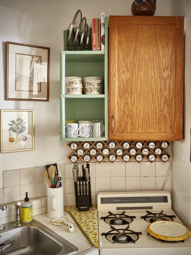 Adjoining kitchen cabinets, one painted green with open shelves. Mounted spice rack below.