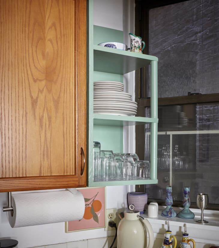 Green open shelf in studio apartment filled with dish ware.
