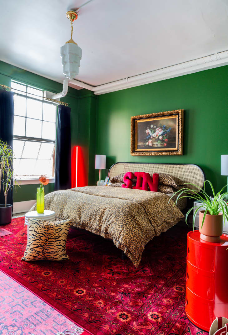 Bedroom with bright deep green walls, red patterned rug, cheetah bed linens, red accents, like throw pillows on the bed that spell SIN, dutch still life style floral painting above bed with ornate gold frame, red neon art, modern decor elements, plants