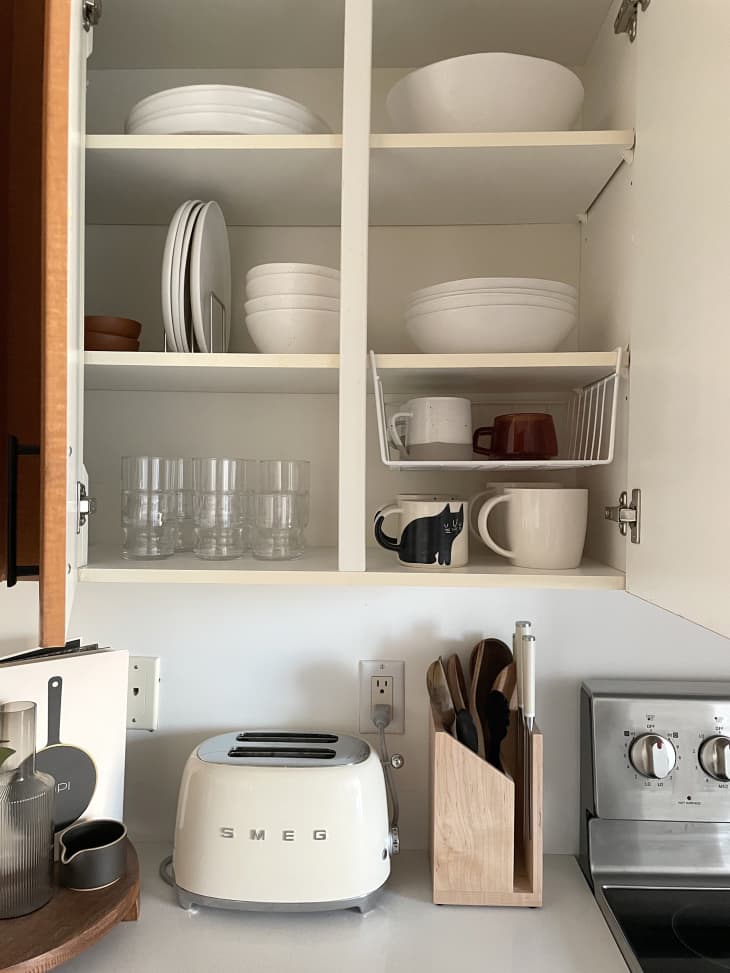 Open kitchen cabinet with white bowls, plates. Glasses and mugs. Counter with smeg toaster, knife block