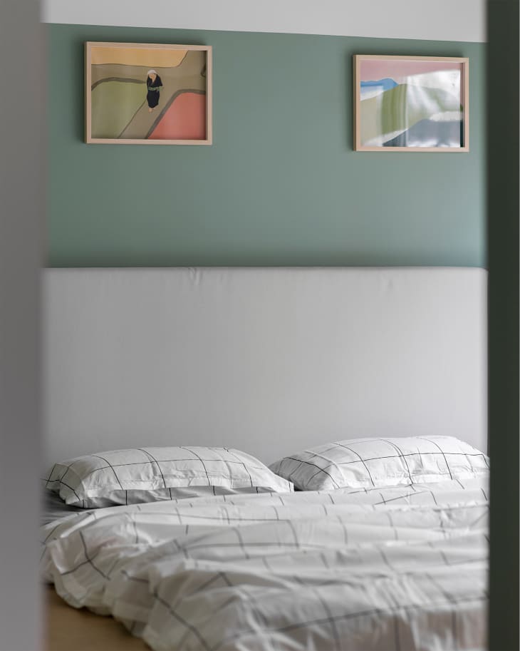 Two pieces of framed art on a green wall over the bed