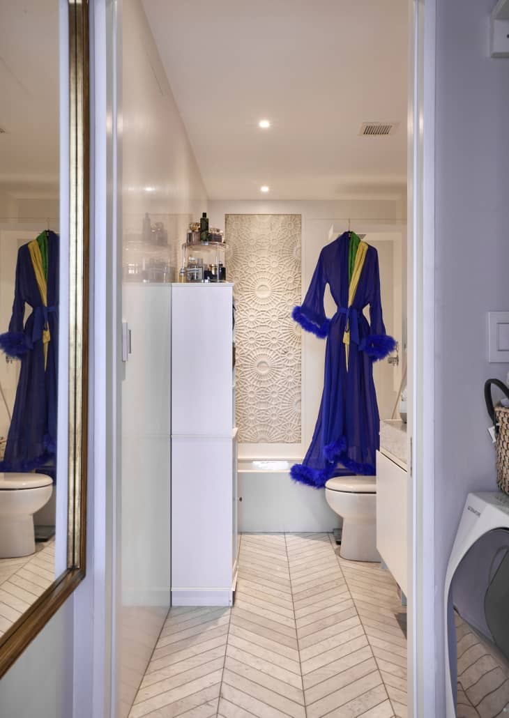 A blue robe hangs on a glass shower curtain in a bathroom with tile.
