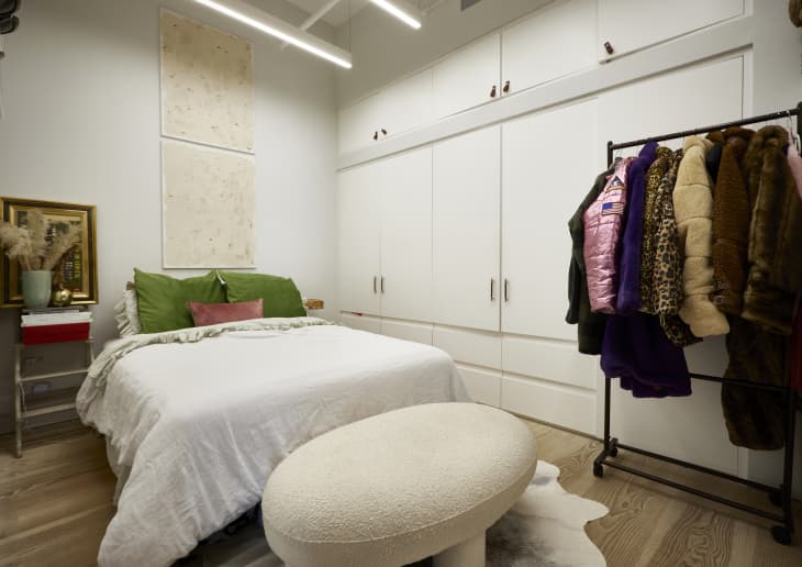 A white bedroom with wall wall-sized built-in closet across from the bed with green and pink pillows.