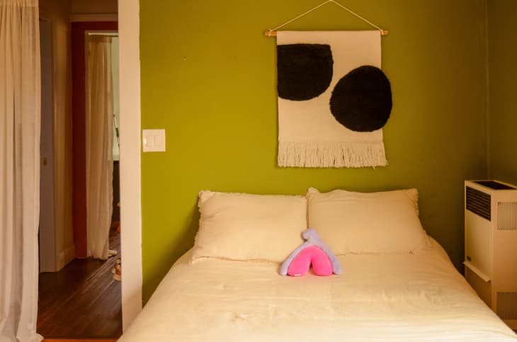 Green accent wall with fabric art above a bed.