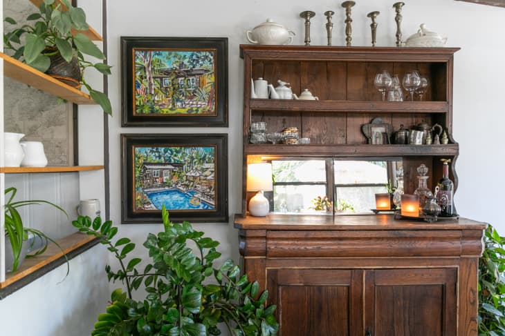 Large wood cabinet and shelves with plants and art around