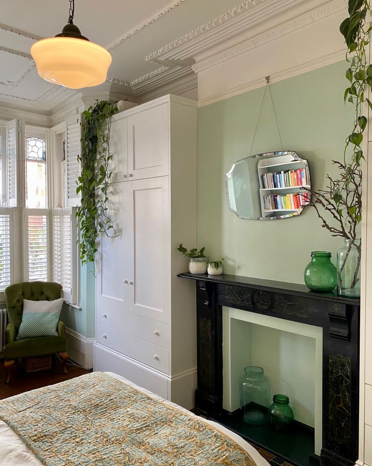 Mirror hanging over fireplace mantel in green painted bedroom.