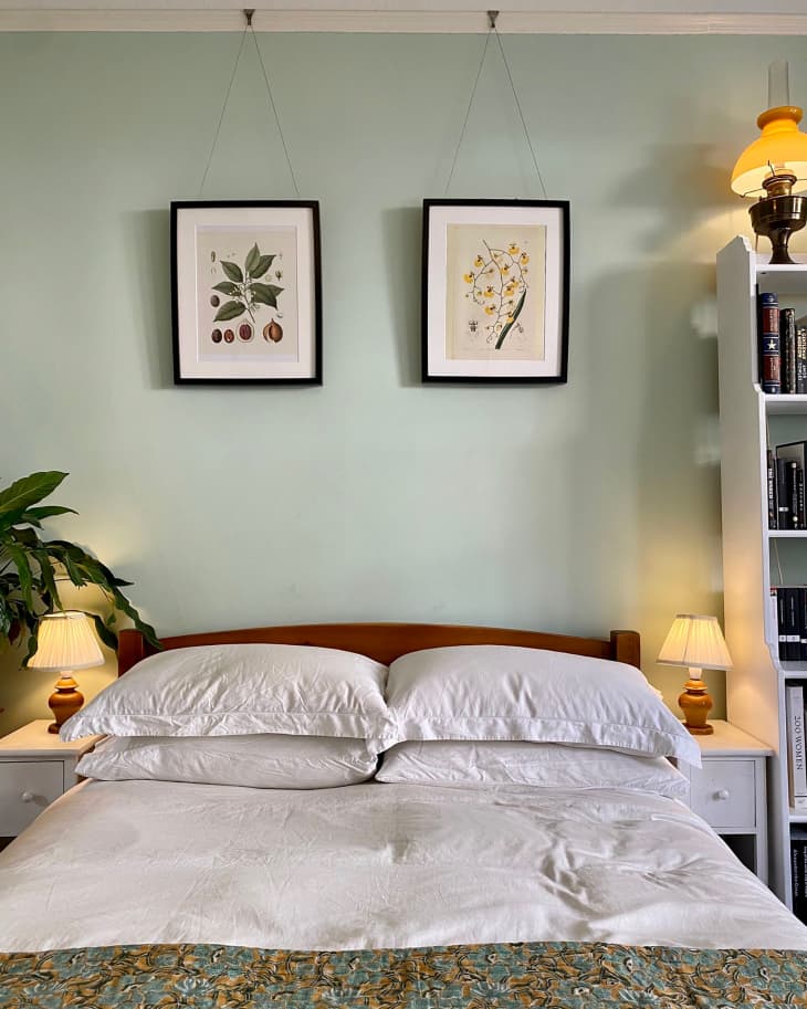 Botanical art prints mounted above bed in green painted bedroom.