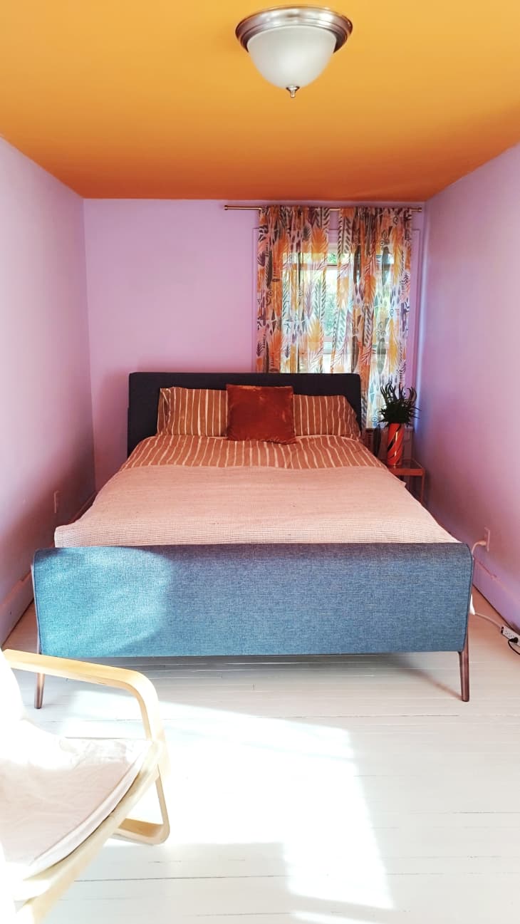 A bed in a nook with purple walls and an orange ceiling decorated with orange pillows.