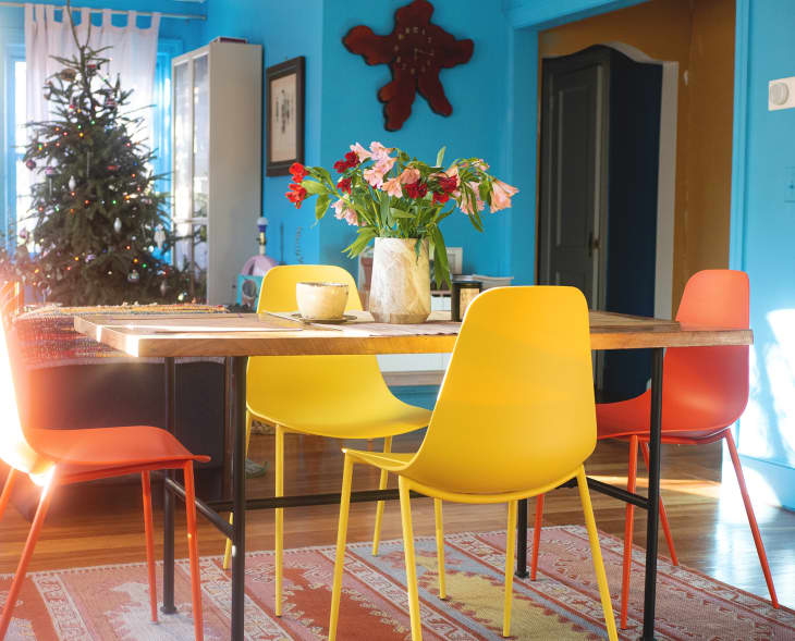 A dining room table circle with yellow and orange chairs in a blue room.