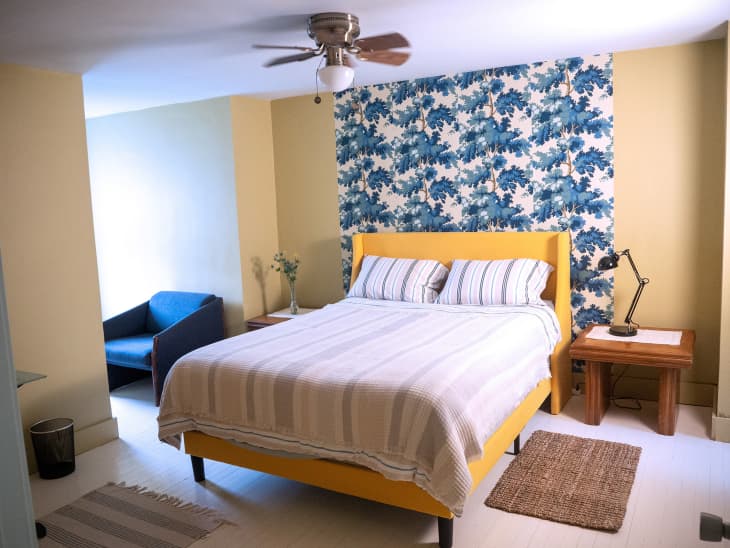 A bed with a yellow bedstand against a floral accent wall.
